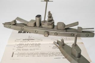 Battaglia navale autarchica. Giocattolo autarchico brevettato, incrociatore e sommergibile “Per procedere alla battaglia navale, appoggiare su di un piano l’incrociatore col bottone grilletto in avanti, collocando ad opportuna distanza il sommergibile col siluro verso l’incrociatore. Tenere fermo il sommergibile con una mano, con l’altra spostare verso destra la boa di salvataggio. Se il tiro è giusto, il siluro colpisce il bottone grilletto dell’incrociatore e questo salta in aria.”