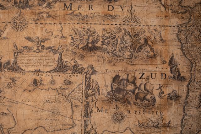 L’immagine raffigura l’angolo inferiore sinistro della mappa in cui si vedono una scena allegorica, alcune imbarcazioni e l’ingrandimento di un dettaglio geografico.